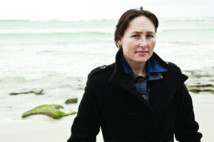 middle aged woman in a black coat standing by a rocky shore